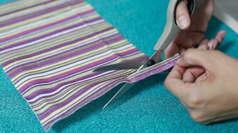 Tesoura recortando uma tira de tecido para cobrir a lateral da tampinha.